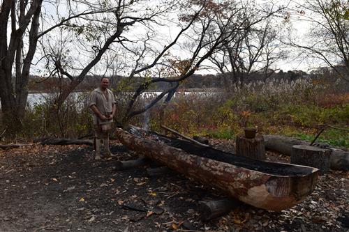 A Wampanoag descendant burning a canoe. 